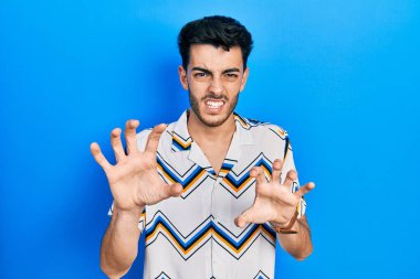 Gündelik kıyafetler giyen genç İspanyol adam komik gülüyor kedi gibi pençe hareketi yapıyor, agresif ve seksi bir ifade. 