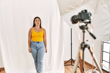 Young beautiful hispanic woman posing as model at photography studio making fish face with lips, crazy and comical gesture. funny expression. 