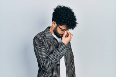 Young arab man with beard wearing glasses tired rubbing nose and eyes feeling fatigue and headache. stress and frustration concept. 
