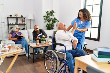 Orta yaşlı doktor kadın ve emekli adam huzurevinde tekerlekli sandalyede beşlik çakıyor..