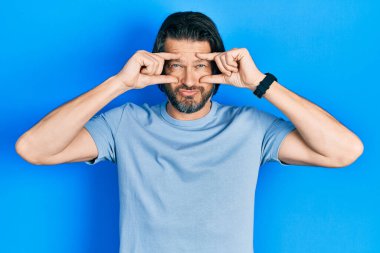 Orta yaşlı, günlük kıyafetler giyen, parmaklarıyla gözlerini açmaya çalışan, uykulu ve yorgun bir beyaz adam. 