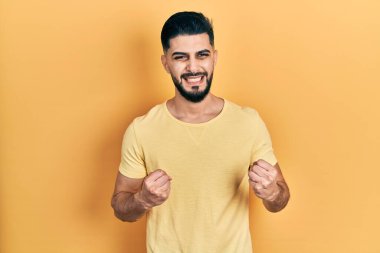 Sarışın sakallı yakışıklı adam başarı için heyecanlı kolları havada ve gözleri kapalı zaferi kutlarken gülümsüyor. Kazanan konsept. 