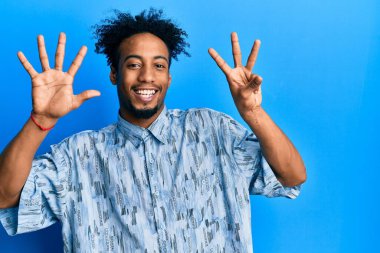 Sakallı, sıradan giyinmiş, 8 numaralı parmaklarıyla gösteriş yapan, kendinden emin ve mutlu gülümseyen Afro-Amerikalı genç adam.. 