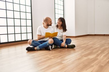 Genç İspanyol çift gülümsüyor boş evde mutlu bir kitap okuyor..
