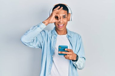 Genç Afrikalı Amerikalı adam akıllı telefon kullanıyor. Kulaklık takıyor. Gülümsüyor. 