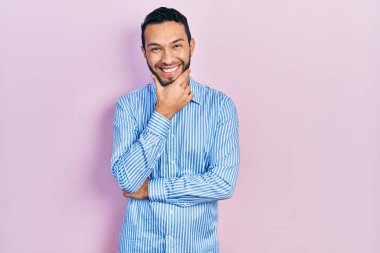 Sakallı, sıradan mavi tişörtlü İspanyol adam kameraya kendinden emin bir şekilde bakıyor. Kollarını kavuşturup, çenesini kaldırarak gülümsüyor. Olumlu düşünmek. 