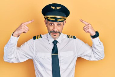 Handsome middle age man with grey hair wearing airplane pilot uniform smiling pointing to head with both hands finger, great idea or thought, good memory 