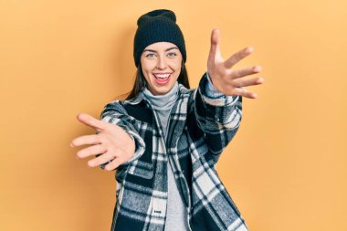 Mavi gözlü, yün şapkalı güzel bir kadın kameraya bakıyor. Sarılmak için kollarını açmış gülümsüyor. Mutluluğu kucaklayan neşeli bir ifade.. 