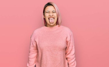 Pembe saçlı, sıradan bir kazak giyen İspanyol kadın komik bir ifadeyle dilini dışarı çıkartıyor. duygu kavramı. 