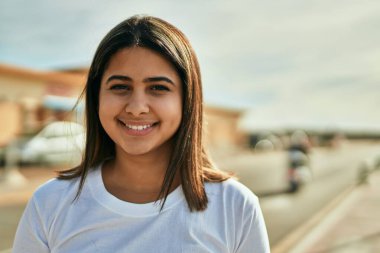 Genç Latin kız gülümseyerek şehirde mutlu mesut dikiliyor..