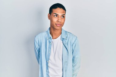 Genç Afro-Amerikalı, günlük kıyafetler giymiş, gülümseyen, yan tarafa bakan ve düşünen.. 