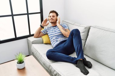 Genç İspanyol adam evde müzik dinlerken kendinden emin gülümsüyor.