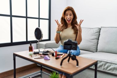 Orta yaşlı İspanyol kadın evinde akıllı telefonuyla makyaj yapıyor zaferi mutlu bir gülümsemeyle kutluyor ve kazanan el kaldırarak ifade ediyor. 