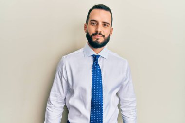 Sakallı, iş kravatlı, yüzünde ciddi bir ifade olan genç bir adam. Basit ve doğal bir şekilde kameraya bakıyorsun.. 