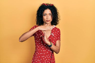 Yazlık elbise giyen genç Latin kız. El kol hareketleri yapıyor, hayal kırıklığına uğramış ve ciddi bir yüz ifadesi takınıyor. 