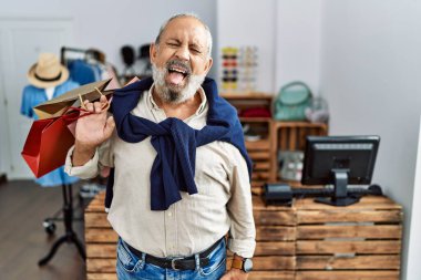 Butik dükkanında alışveriş torbaları tutan yakışıklı bir adam komik bir ifadeyle dilini dışarı çıkartıyor. duygu kavramı. 