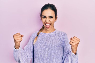 Gündelik giysiler giyen genç İspanyol kız kollarını kaldırıp, gözleri açık bir şekilde başarıyı kutluyor ve şaşırıyor. Kazanan konsept. 