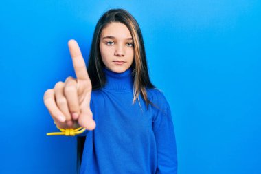 Balıkçı yaka kazak giyen genç esmer kız parmağını kaldırmış ve kızgın bir ifadeyle işaret ediyor. 