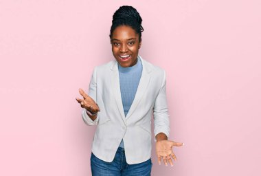 Genç Afro-Amerikan kadın iş kıyafetleri içinde neşeli bir şekilde kollarını açıp gülümsüyor. Hoş geldin, olumlu ve kendinden emin selamlar. 