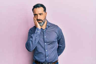 Sakallı, gri saçlı, iş kıyafetleri giyen orta yaşlı bir adam kollarını kavuşturarak depresyondan sıkılmış ve yorgun göründüğünü düşünüyor.. 