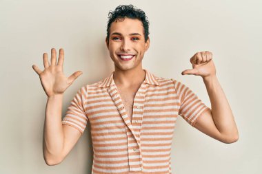 Handsome man wearing make up wearing casual t shirt showing and pointing up with fingers number six while smiling confident and happy. 