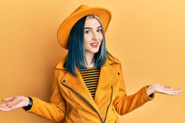 Sarı şapkalı ve deri ceketli genç modern kız gülümseyerek avuçlarını açıyor, sunuyor ve reklam karşılaştırması yapıyor ve dengeyi sağlıyor. 