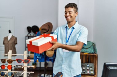 Young hispanic man working as shop assistant selling gift at retail shop