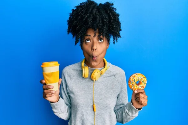 黑头发的非洲裔美国女人吃甜甜圈 喝咖啡 用嘴和眼神做鱼脸 疯狂而滑稽 — 图库照片