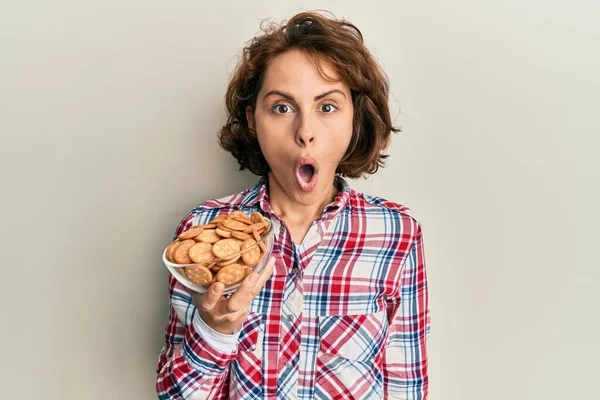 Young Brunette Woman Holding Bowl Salty Biscuits Scared Amazed Open — Stock Photo, Image