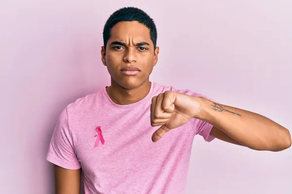 年轻英俊的他的惊慌失措的男人穿着粉红的癌症带衬衫 满脸怒容 消极的迹象显示不喜欢大拇指朝下 拒绝的概念 — 图库照片