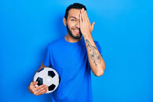 Латиноамериканець Бородою Тримає Футбольний Закриваючи Одне Око Рукою Впевненою Посмішкою — стокове фото