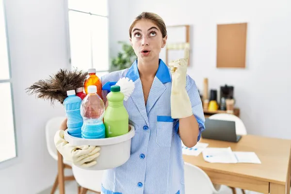 Jovem Loira Vestindo Uniforme Limpeza Segurando Produtos Limpeza Espantados Surpresos — Fotografia de Stock