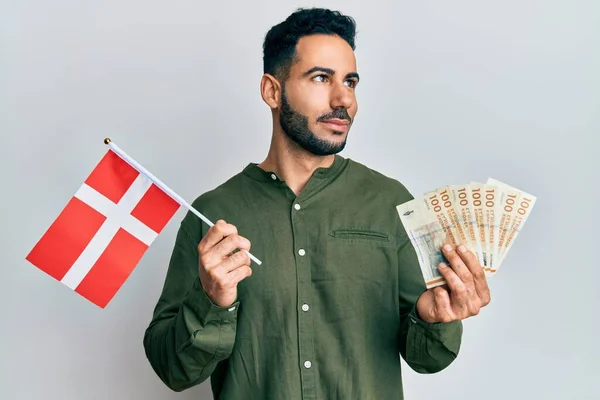 Young Hispanic Man Holding Denmark Flag Krone Banknotes Smiling Looking — Zdjęcie stockowe