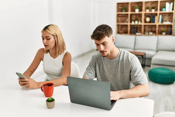 年轻的高加索夫妇在家里喝咖啡 使用笔记本电脑和智能手机 — 图库照片