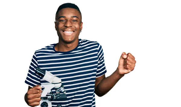 Joven Hombre Afroamericano Sosteniendo Microscopio Gritando Orgulloso Celebrando Victoria Éxito —  Fotos de Stock