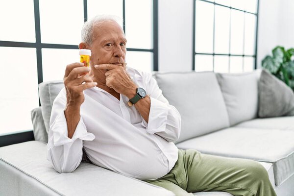 Senior man holding pills looking confident at the camera smiling with crossed arms and hand raised on chin. thinking positive. 