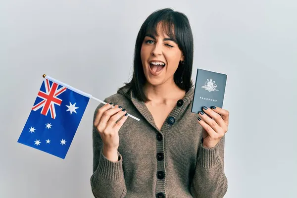 Young hispanic woman holding australian flag and passport winking looking at the camera with sexy expression, cheerful and happy face. — Stock Image Young Hispanic Woman Holding Australian Flag Passport Winking Looking Camera Royalty Free Stock Photos