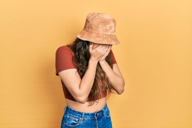 Günlük kıyafetler giyen ve ağlarken yüzünü ellerle kapatan üzgün yüzlü bir şapka takan genç İspanyol kız. depresyon kavramı. 