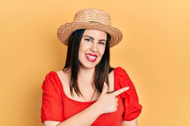 Genç İspanyol kadın yaz şapkası takıyor. Neşeli. Yüzünde mutlu ve doğal bir ifadeyle elleri ve parmaklarıyla gülümsüyor. 