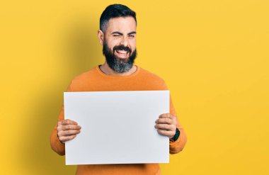 Sakallı, boş pankart taşıyan, seksi bir ifadeyle kameraya bakan, neşeli ve mutlu yüzlü İspanyol bir adam.. 