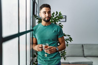 Genç Arap adam evde çay içerek kendinden emin gülümsüyor.