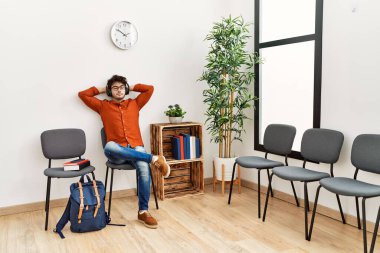 Genç İspanyol adam, bekleme odasında müzik dinlerken kendinden emin bir şekilde gülümsüyor.