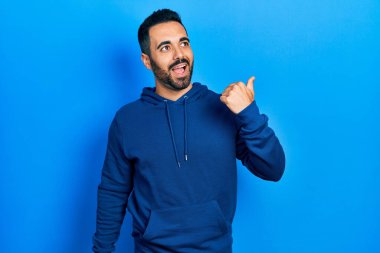 Yakışıklı, sakallı, sıradan bir kazak giyen, başparmağını kaldırıp gülümseyen, ağzı açık bir İspanyol. 