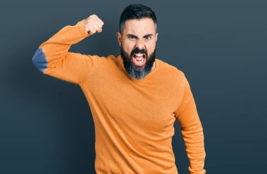Hispanic man with beard wearing casual winter sweater angry and mad raising fist frustrated and furious while shouting with anger. rage and aggressive concept. 