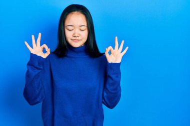 Günlük kıyafetler giyen genç Çinli kız rahatla ve gözleri kapalı gülümse parmaklarıyla meditasyon hareketi yapıyor. yoga konsepti. 