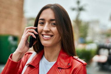 Genç İspanyol kadın gülümsüyor. Şehirdeki akıllı telefondan konuşuyor..