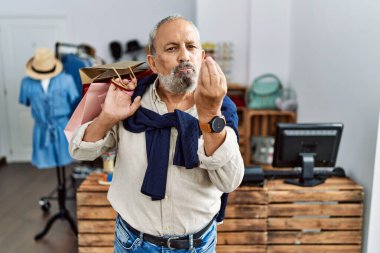 Yakışıklı son sınıf öğrencisi butik dükkanında alışveriş torbaları tutuyor. İtalyan jestleri yapıyor. Elleri ve parmakları kendinden emin bir ifadeyle. 