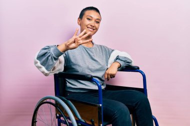 Tekerlekli sandalyede oturan, dört numaralı parmaklarıyla işaret eden, kendinden emin ve mutlu gülümseyen güzel İspanyol kadın.. 