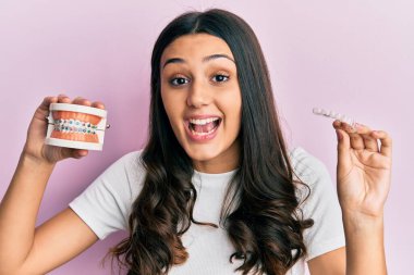 Latin kökenli genç bir kadın, elinde görünmez bir hizacı ve diş teli tutarak çılgınlığı kutluyor ve başarı için hayrete düşüyor.. 