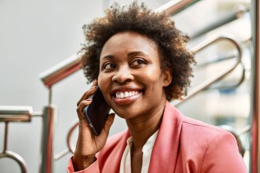Güzel iş kadını afro saçlı Afro-Amerikan kadın mutlu ve kendinden emin bir şekilde şehirde telefonda konuşuyor.